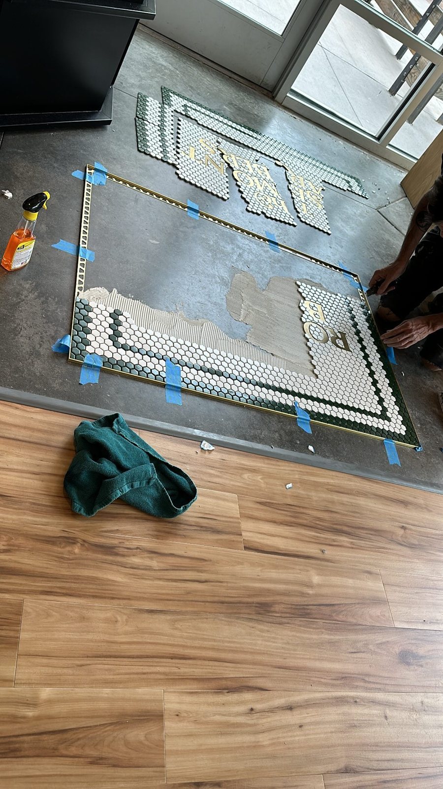 Mosaic sheets with gold metal letters being set into adhesive inside an edge trim