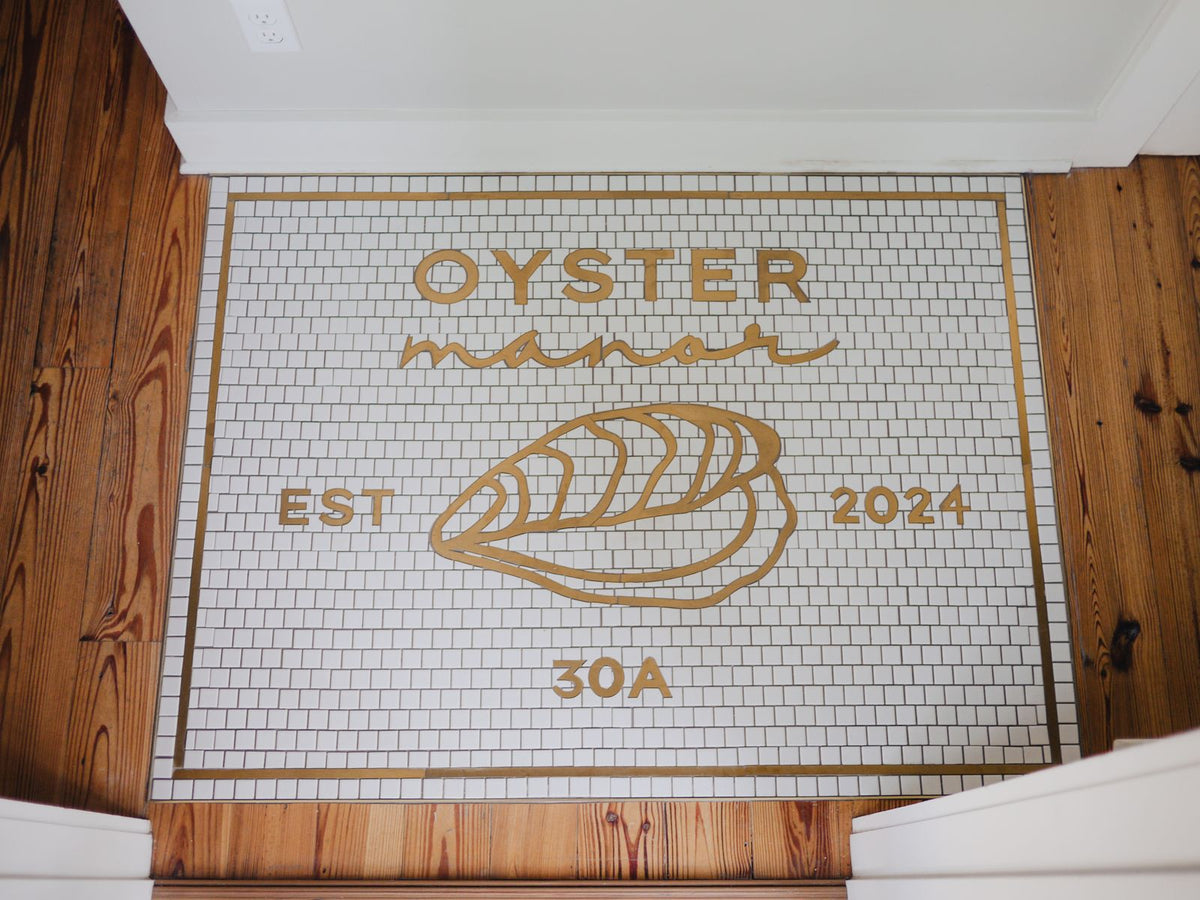 Oyster Manor gold metal logo mosaic set into a wood floor entrance